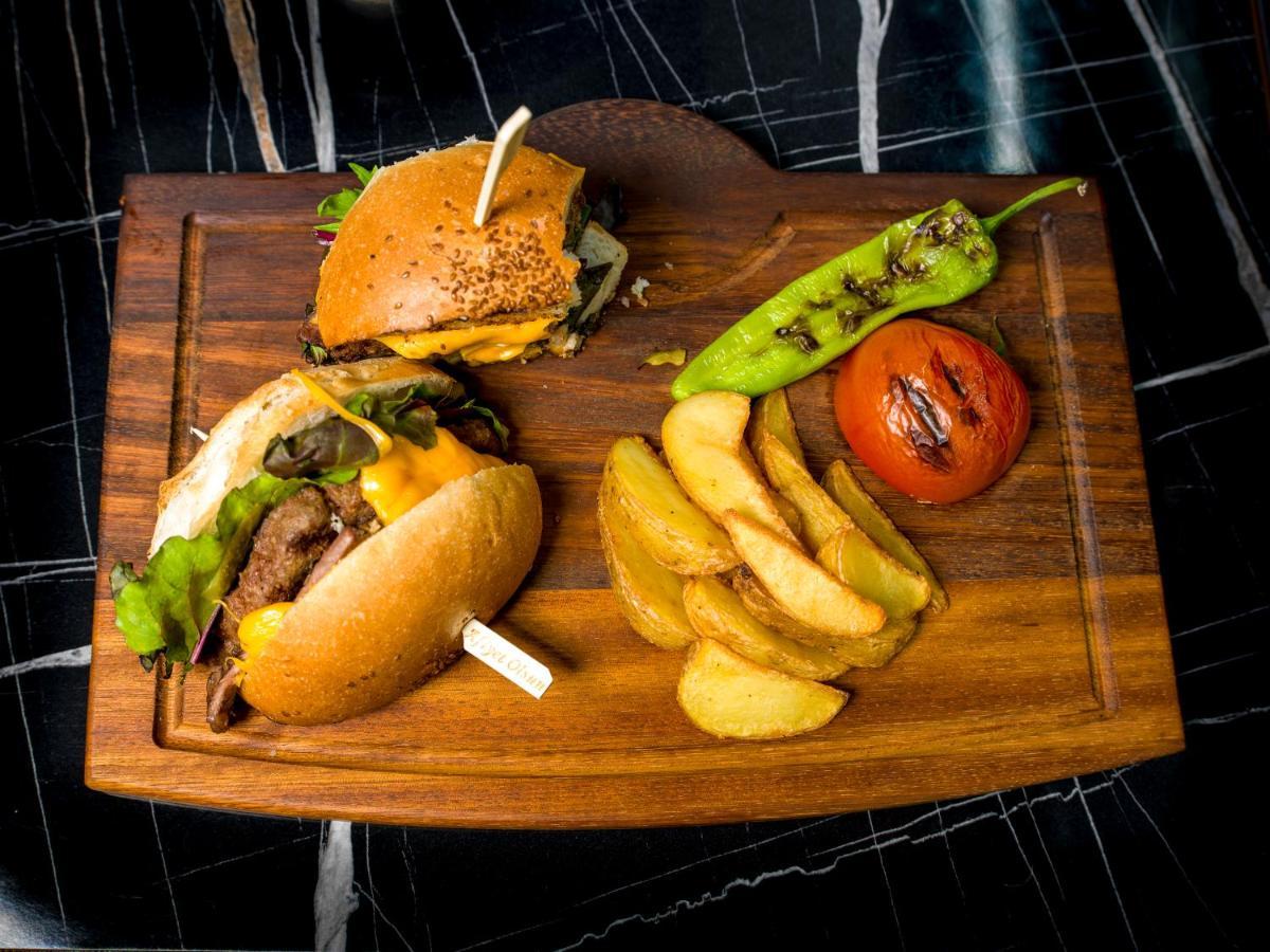 Menalo Hotel Premium Istanbul Airport Екстериор снимка The photo shows a wooden platter featuring a meal that includes two burgers. The first burger is topped with what appears to be lettuce and cheese, while the second burger has a more varied topping. Alongside the burgers, there are golden-brown potat