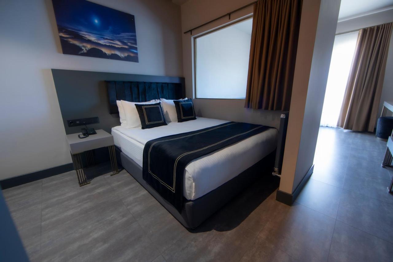Menalo Hotel Premium Istanbul Airport Екстериор снимка The photo shows a modern hotel room featuring a double bed with black and white bedding. There are two decorative pillows on the bed, and behind it is a wall-mounted headboard. To the left of the bed, there's a small bedside table with a lamp. A larg